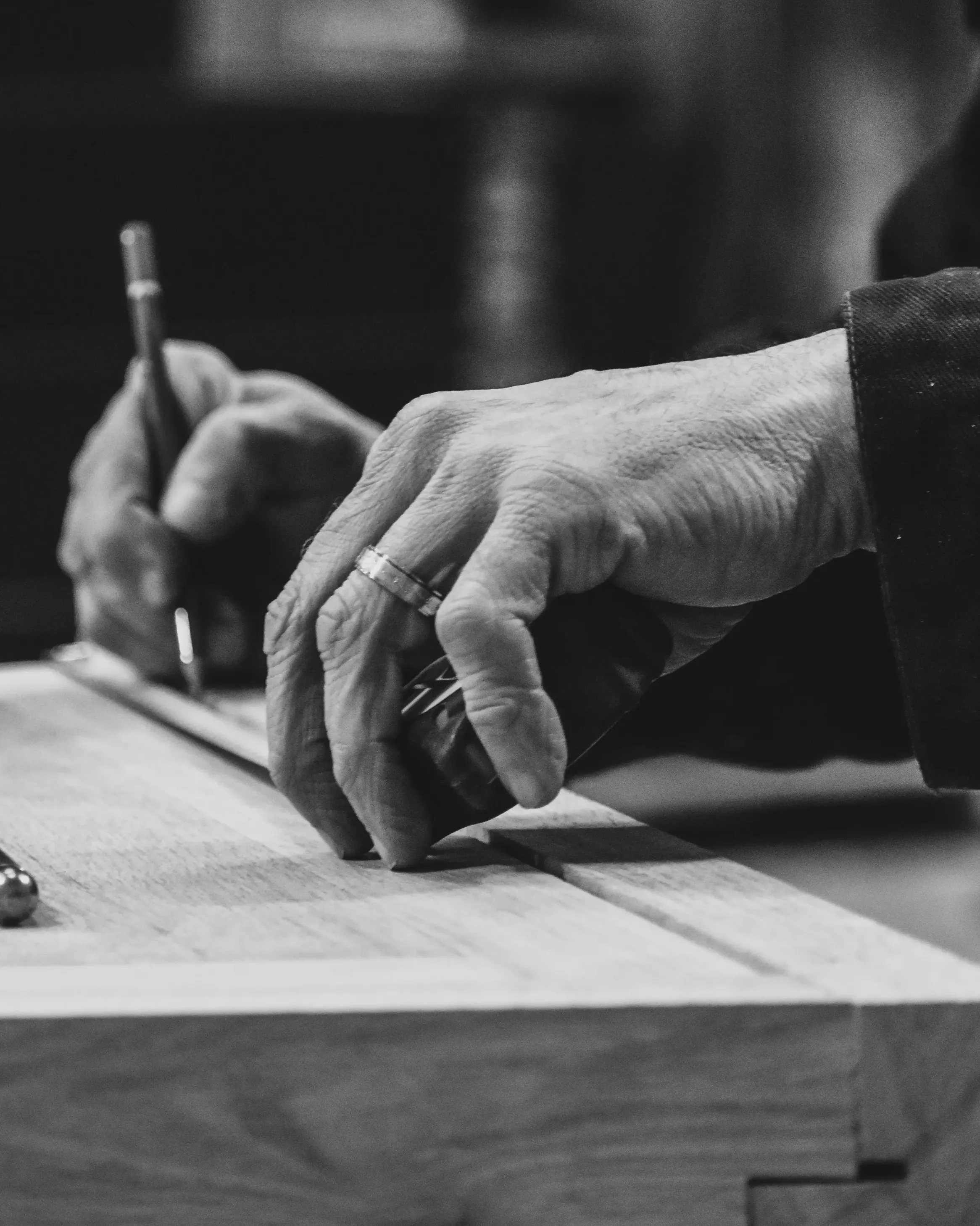 Photo en noir et blanc représentant les mains d'un menuisier utilisant un mètre ruban et un crayon pour mesurer une pièce de bois haut de gamme sur-mesure. Fabrication haut de gamme éternel sur-mesure et éthique Maison Charlet.